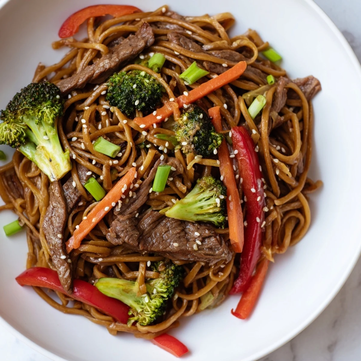 Savory lo mein noodles tossed with beef and broccoli in a glossy, dark sesame-soy sauce, steaming in a skillet.