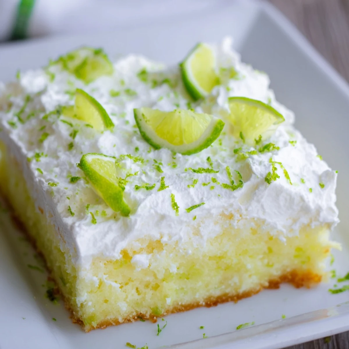 Perfectly set Lime Poke Cake for summer gatherings, topped with velvety whipped cream and sparkling fresh lime zest.