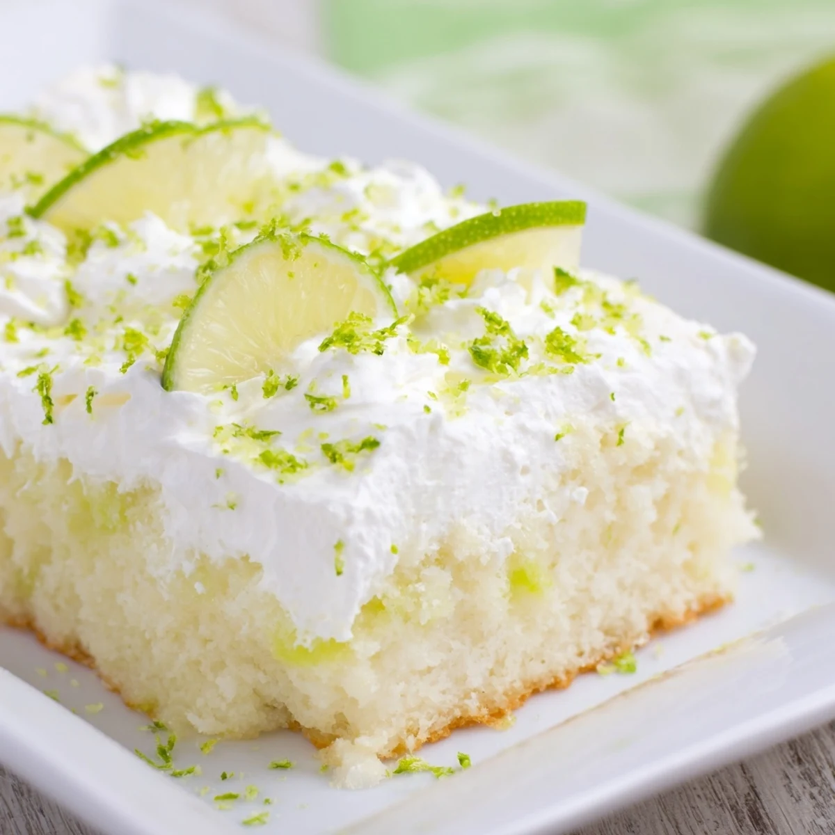 A chilled Lime Poke Cake slice revealing moist, lime-soaked crumb and a cloud of sweet whipped cream topping.