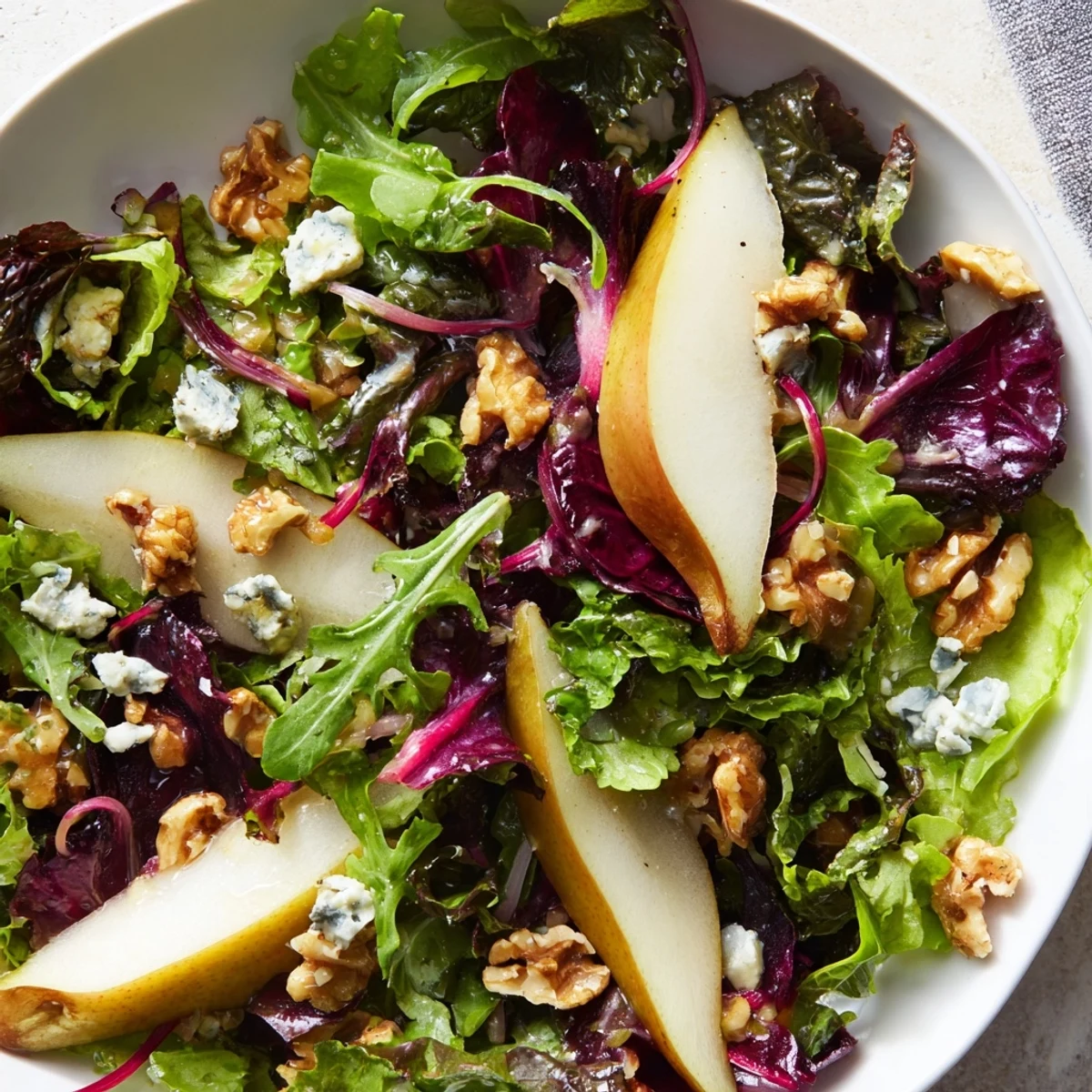 Fresh baby kale and arugula tossed with sliced pears and crunchy toasted walnuts for a Winter Green Salad with Pear and Walnuts.