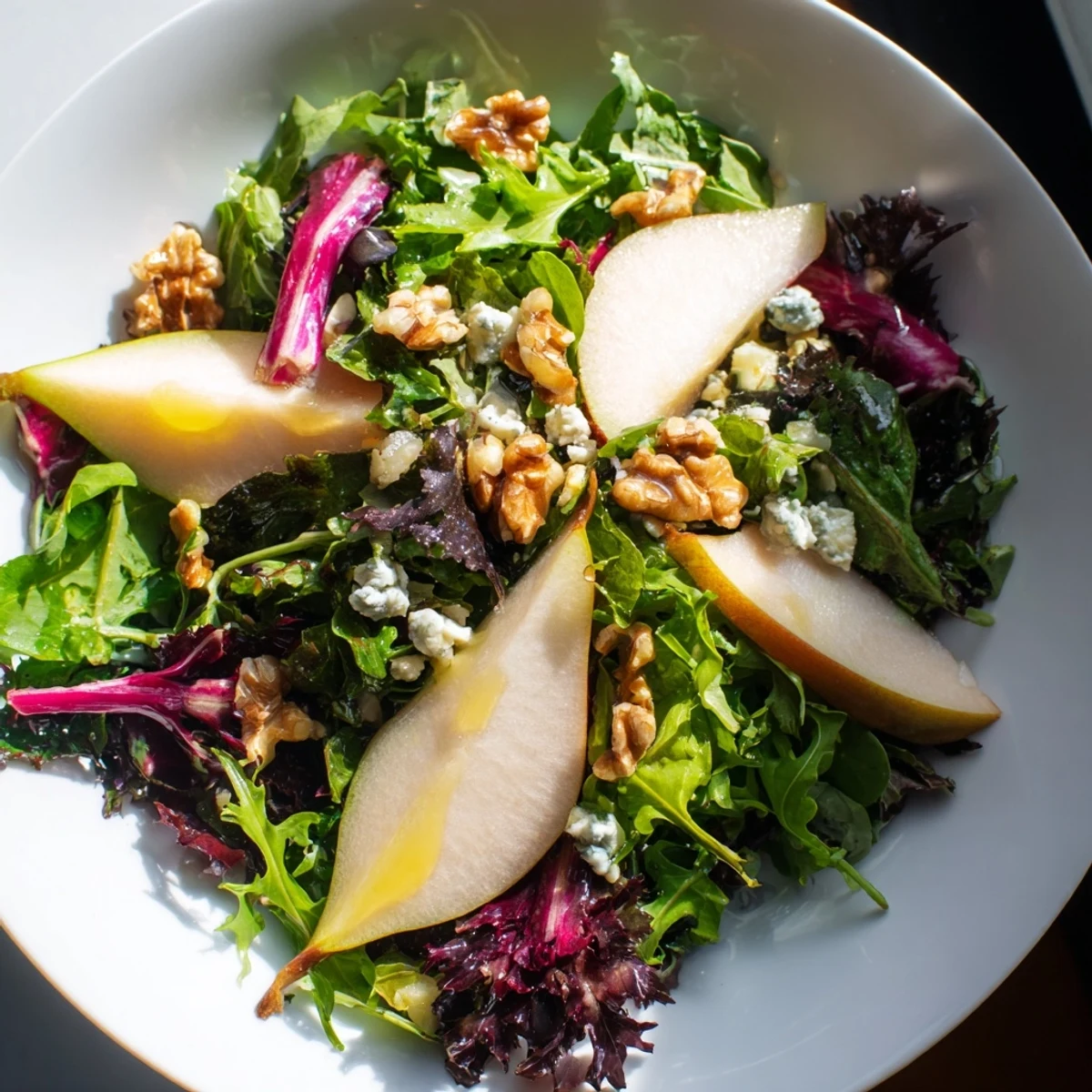 A close-up of Winter Green Salad with Pear and Walnuts topped with crumbled goat cheese and drizzled with tangy vinaigrette.