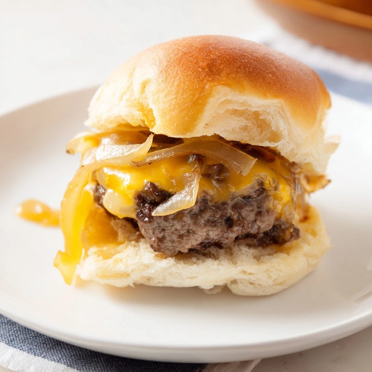 Golden caramelized onions topping mini beef burgers with melted cheese on soft buns.