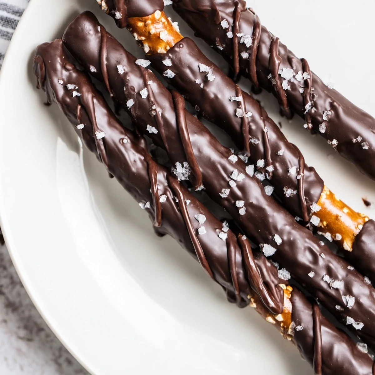 Close-up of Chocolate Dipped Pretzels with Sea Salt, showing thick dark chocolate coating and sparkling salt crystals on a rustic wooden board.