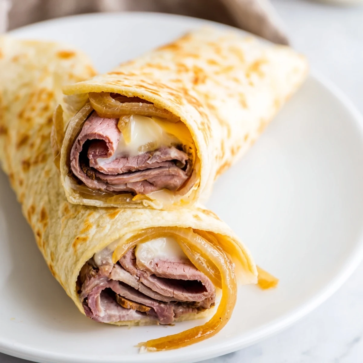 Golden-brown Easy French Dip Tortilla Roll Ups stuffed with roast beef and melted provolone on a white plate.