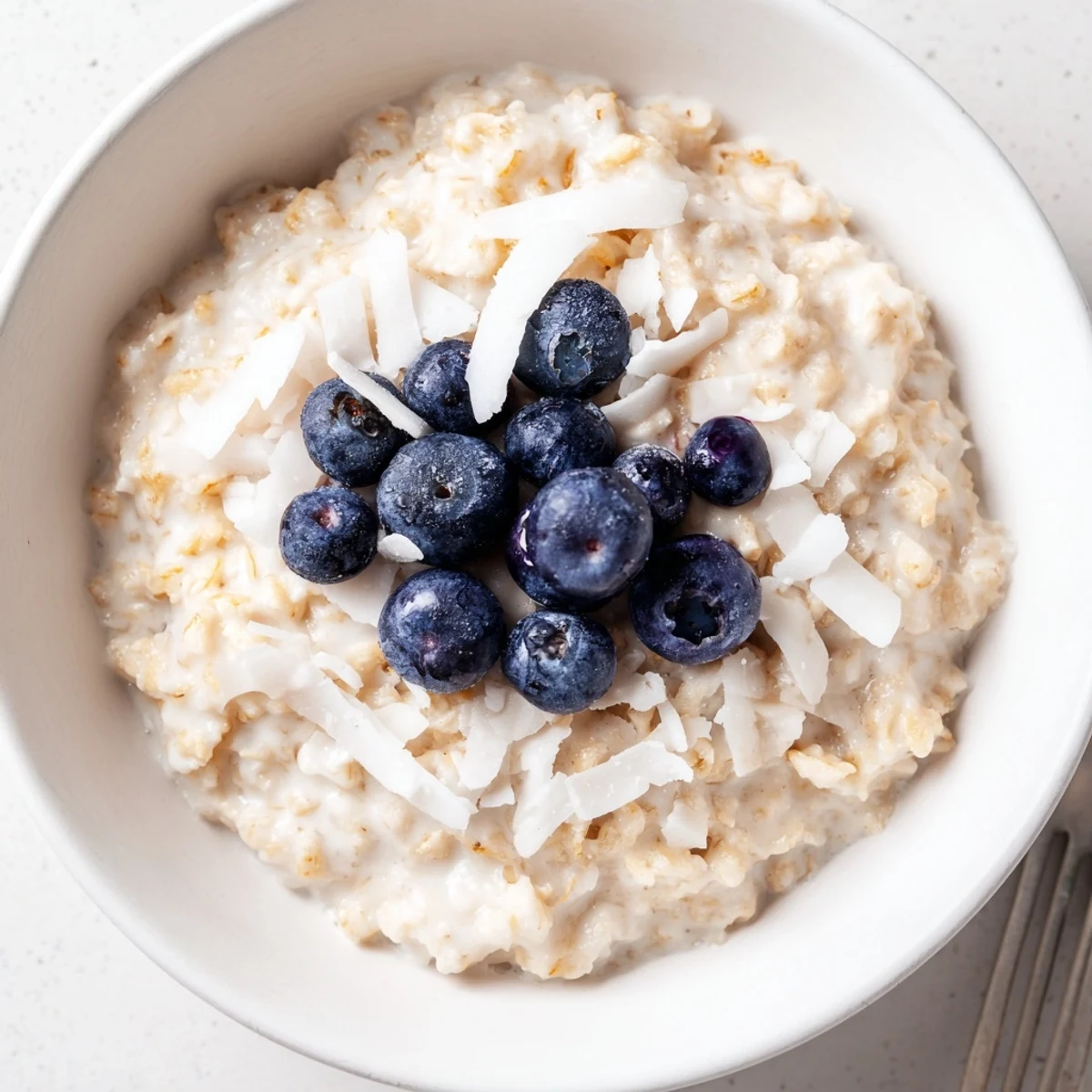 A warm bowl of Tasty Coconut Cream Oats topped with fresh berries and toasted coconut flakes.