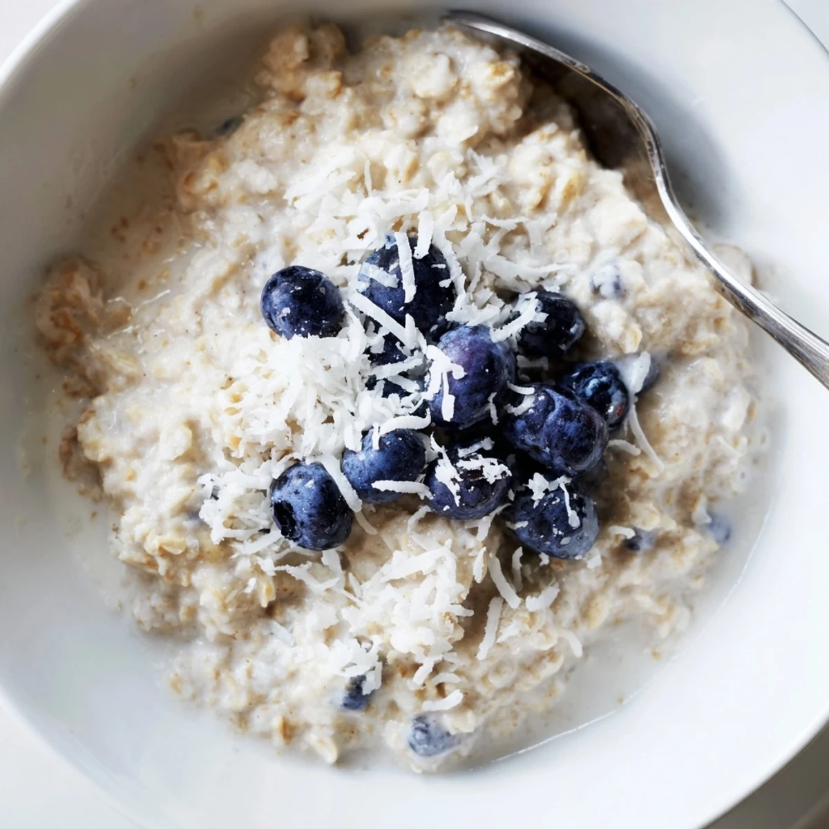 Steaming Tasty Coconut Cream Oats in a white bowl, garnished with chia seeds and sweet fruit.