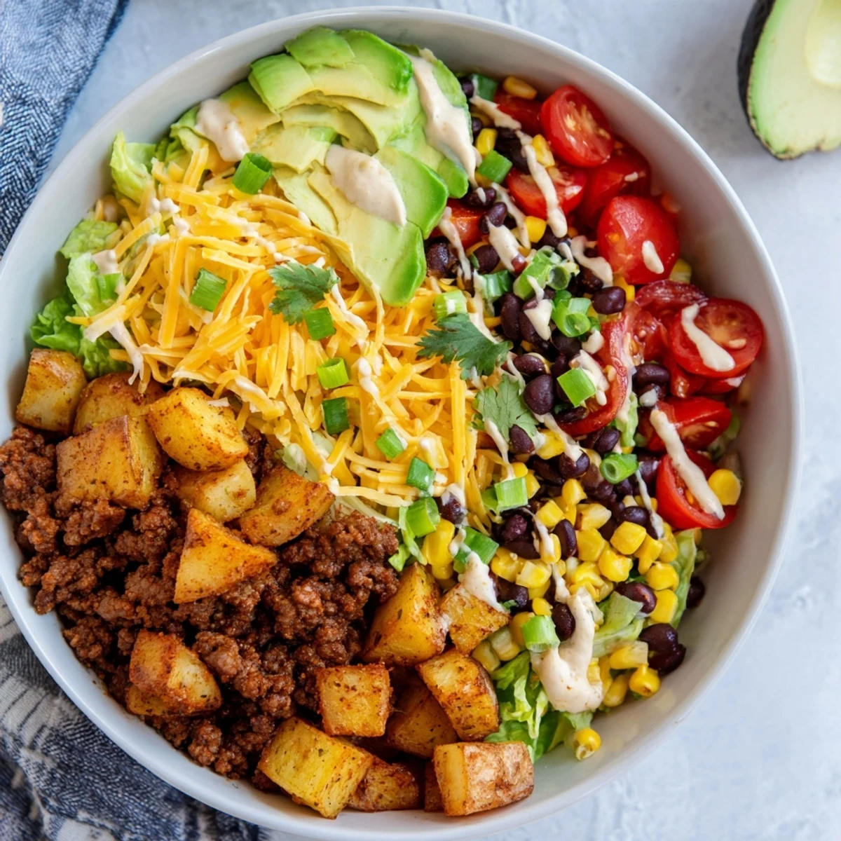 A close-up of a Loaded Potato Taco Bowl featuring crispy potatoes, melted cheddar, and vibrant corn and avocado.