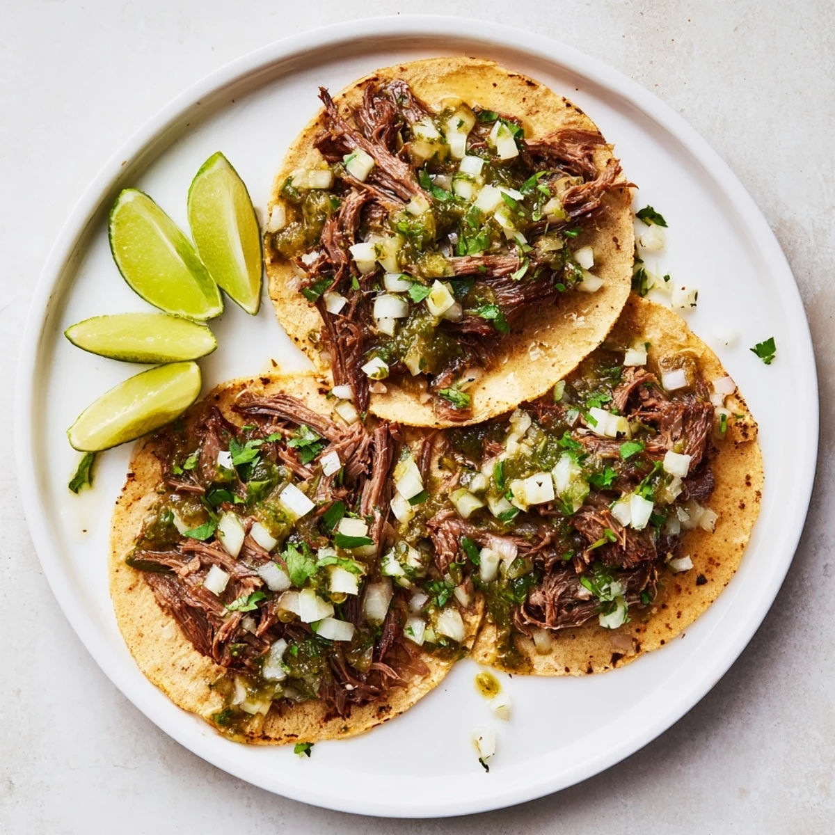 Six savory Beef Cheek Tacos garnished with onion and cilantro, served with lime wedges on a rustic plate.