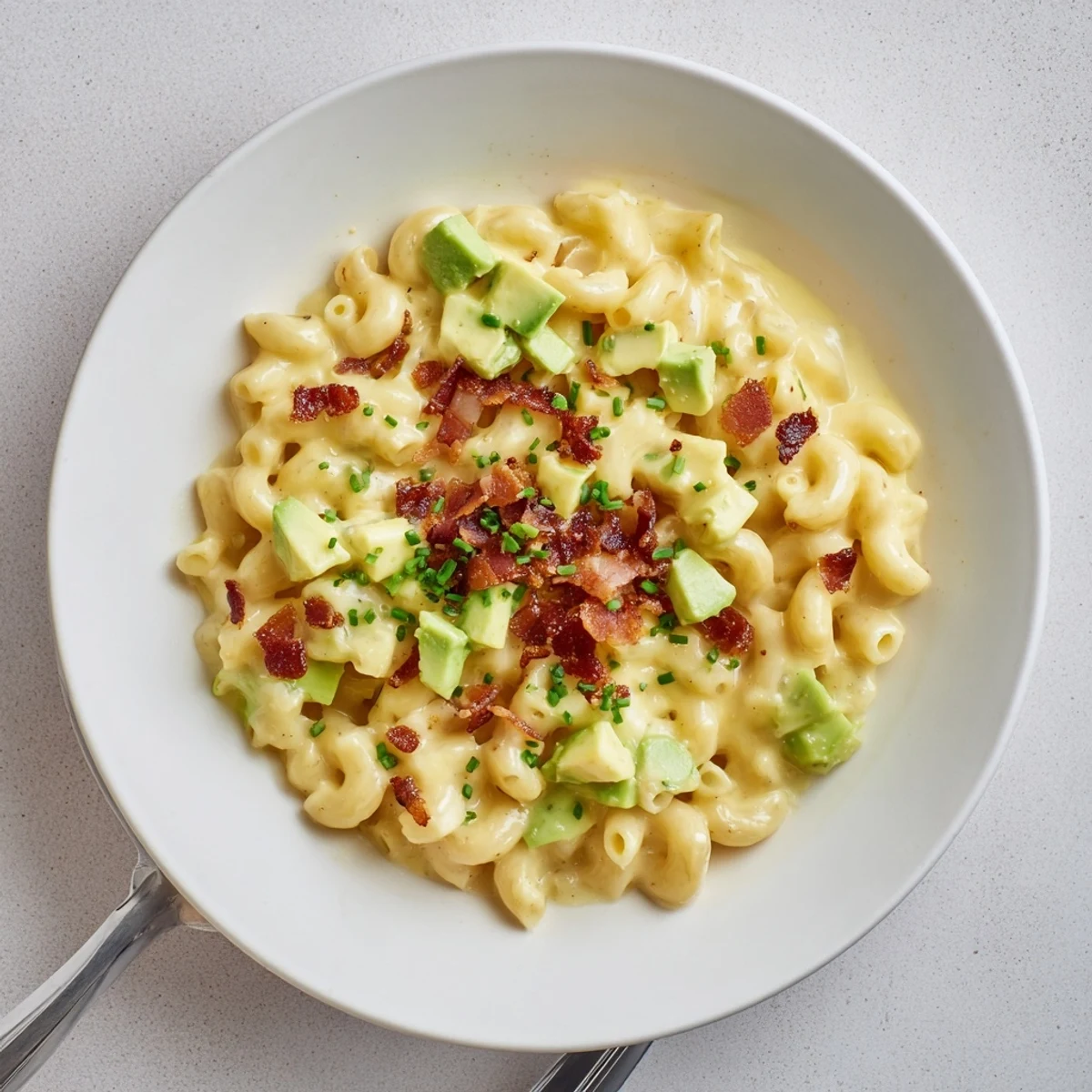 Creamy Avocado and Bacon Mac and Cheese served in a bowl, topped with crispy bacon bits and fresh chives, a fork ready to dig in.