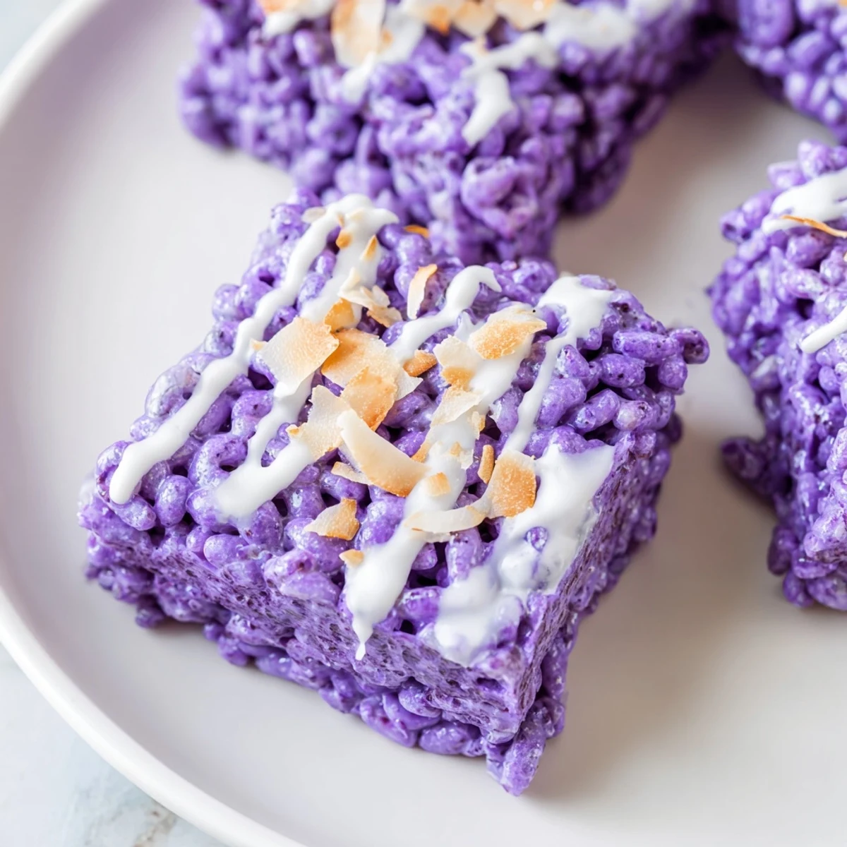 Vibrant purple ube rice krispie treats drizzled with white chocolate and toasted coconut