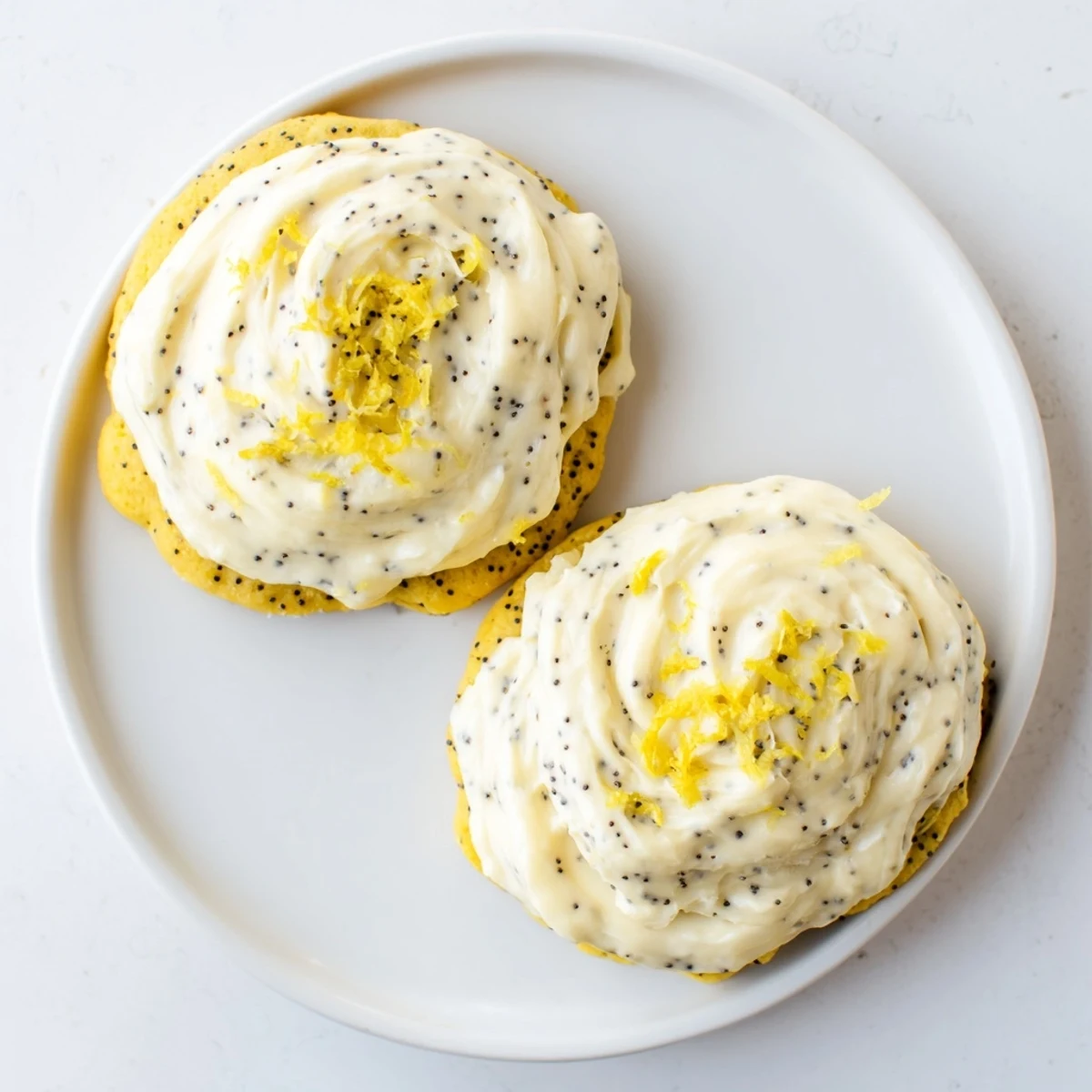 Golden lemon poppy seed cookies with cheesecake frosting on a white serving plate