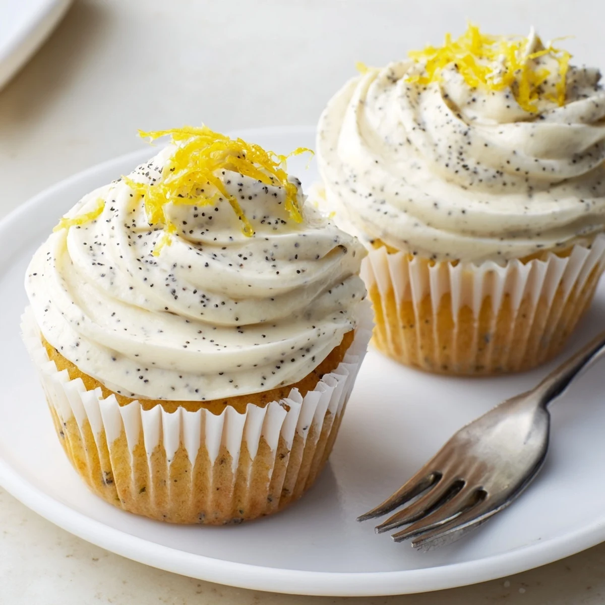 Freshly baked lemon poppy seed cupcakes arranged on a white serving platter with piped cream cheese frosting and extra poppy seed garnish