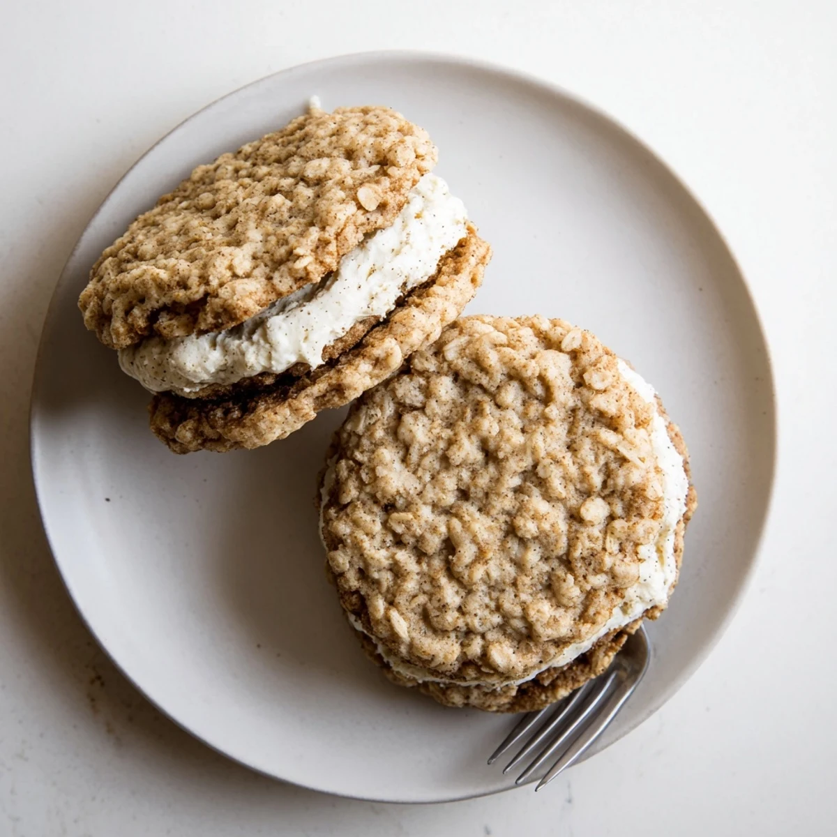 Stack of chewy oatmeal cookies sandwiched with fluffy white cream filling on wooden board
