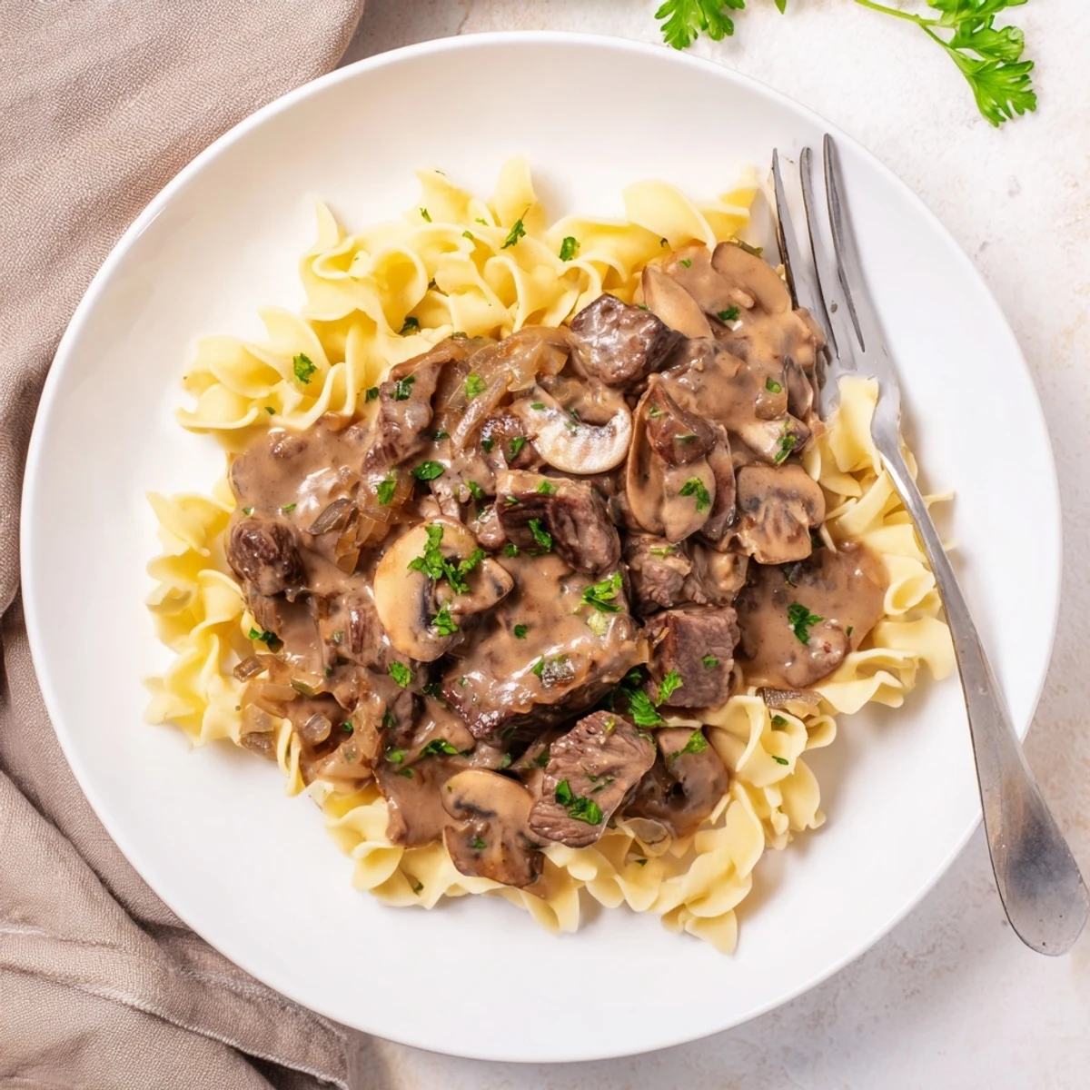 Creamy beef stroganoff with tender beef slices and mushrooms over egg noodles sprinkled with fresh parsley