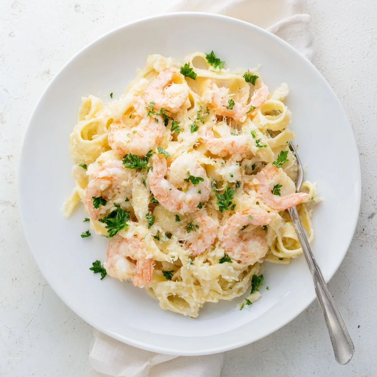 Golden fettuccine noodles coated in velvety Alfredo sauce alongside plump juicy shrimp in a skillet
