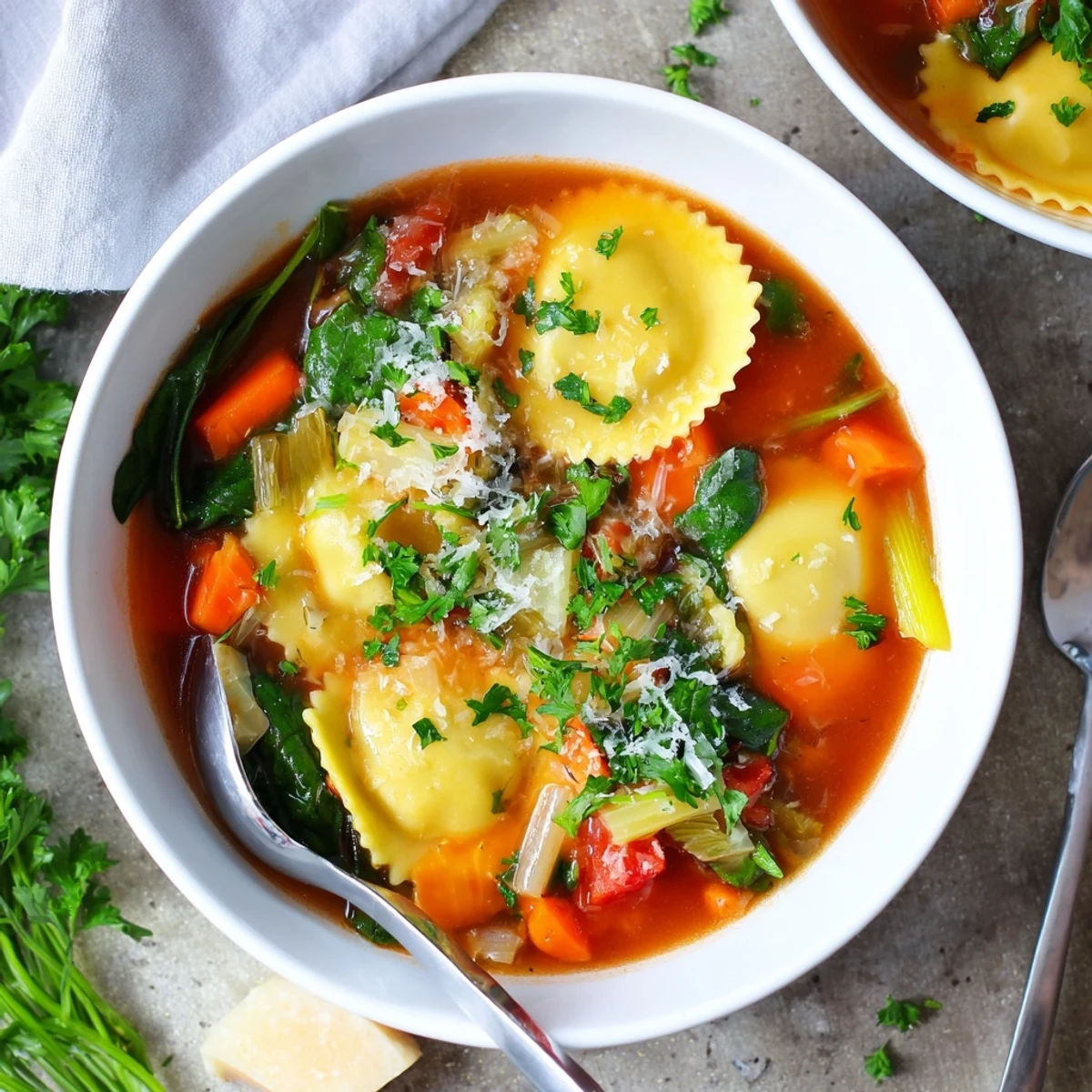 Hearty Easy Tuscan Ravioli Soup featuring plump ravioli, diced vegetables, and wilted spinach garnished with grated Parmesan cheese