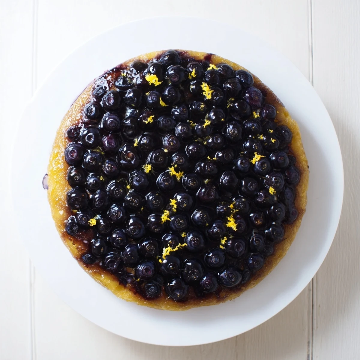 Fresh baked blueberry upside down cake inverted onto a serving platter showing bubbling purple berries