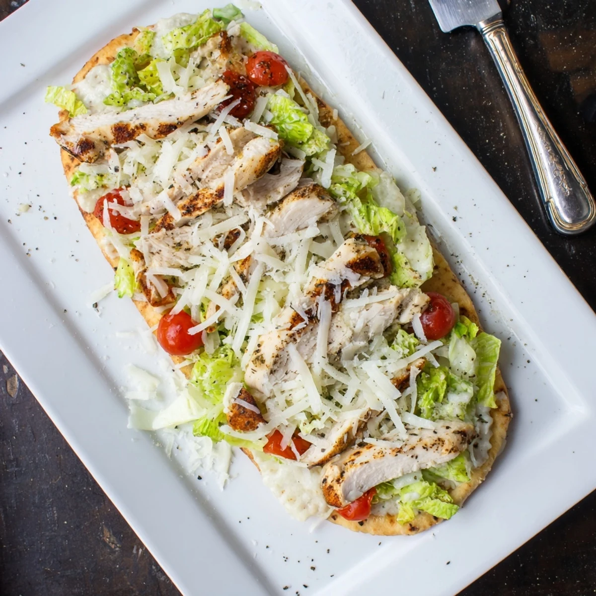 Sliced grilled chicken atop cheesy flatbread piled high with creamy Caesar dressed romaine and fresh cracked pepper