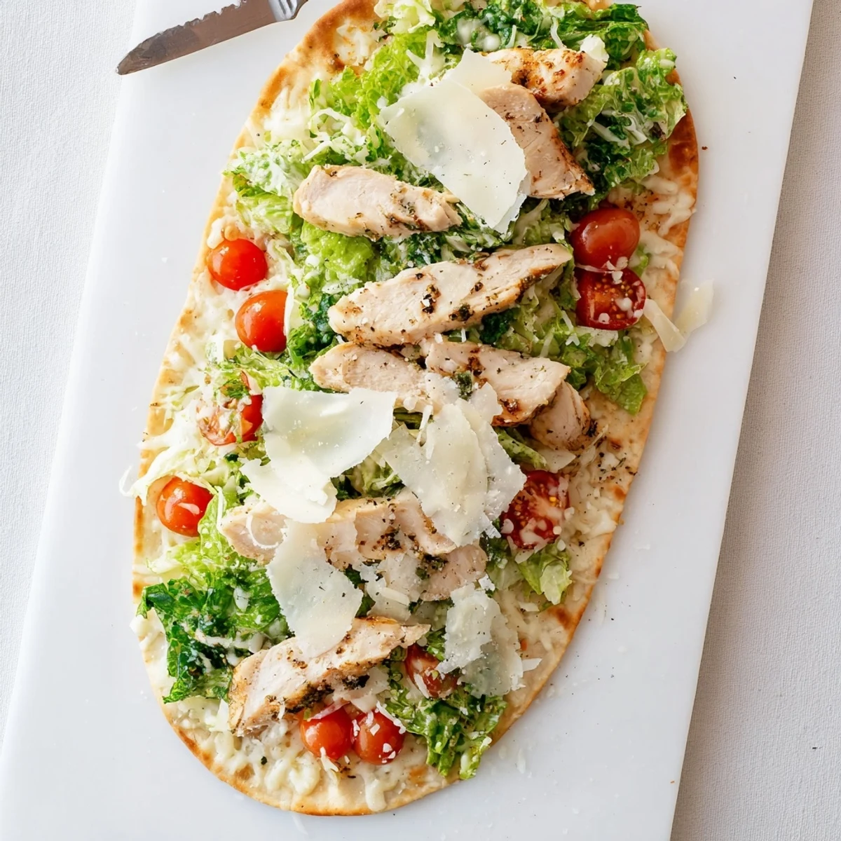 Homemade chicken Caesar flatbread with juicy seasoned chicken breast, bubbly cheese, and crisp lettuce on golden crust