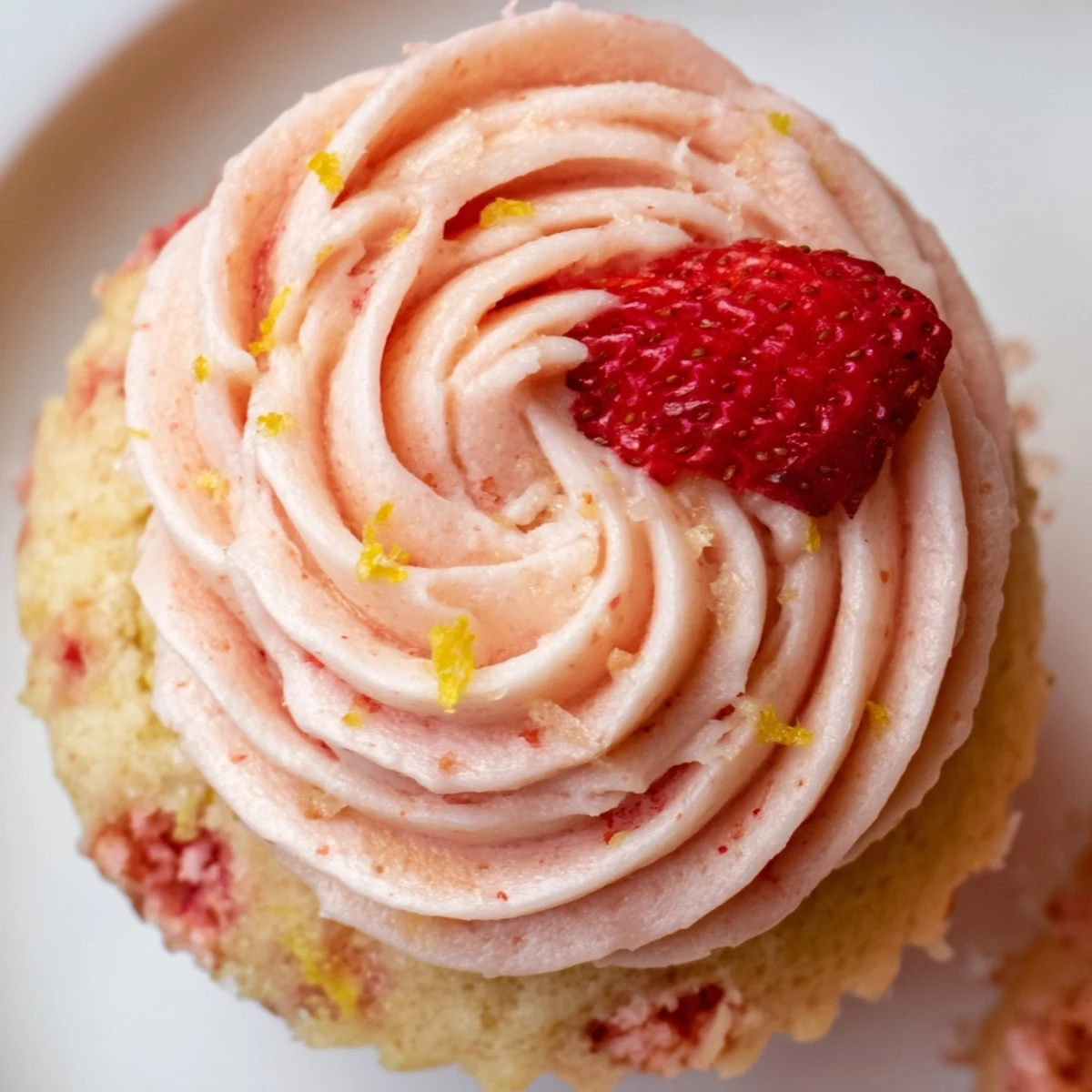 Fresh strawberry lemonade cupcakes with tall fluffy pink frosting piped high and garnished with lemon zest