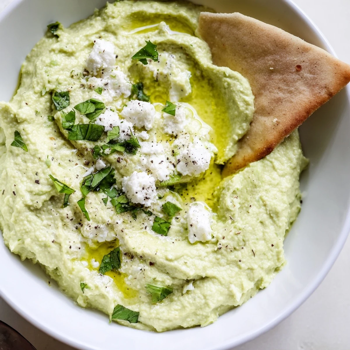 Creamy Avocado Feta Dip spooned into a bowl, surrounded by colorful veggies