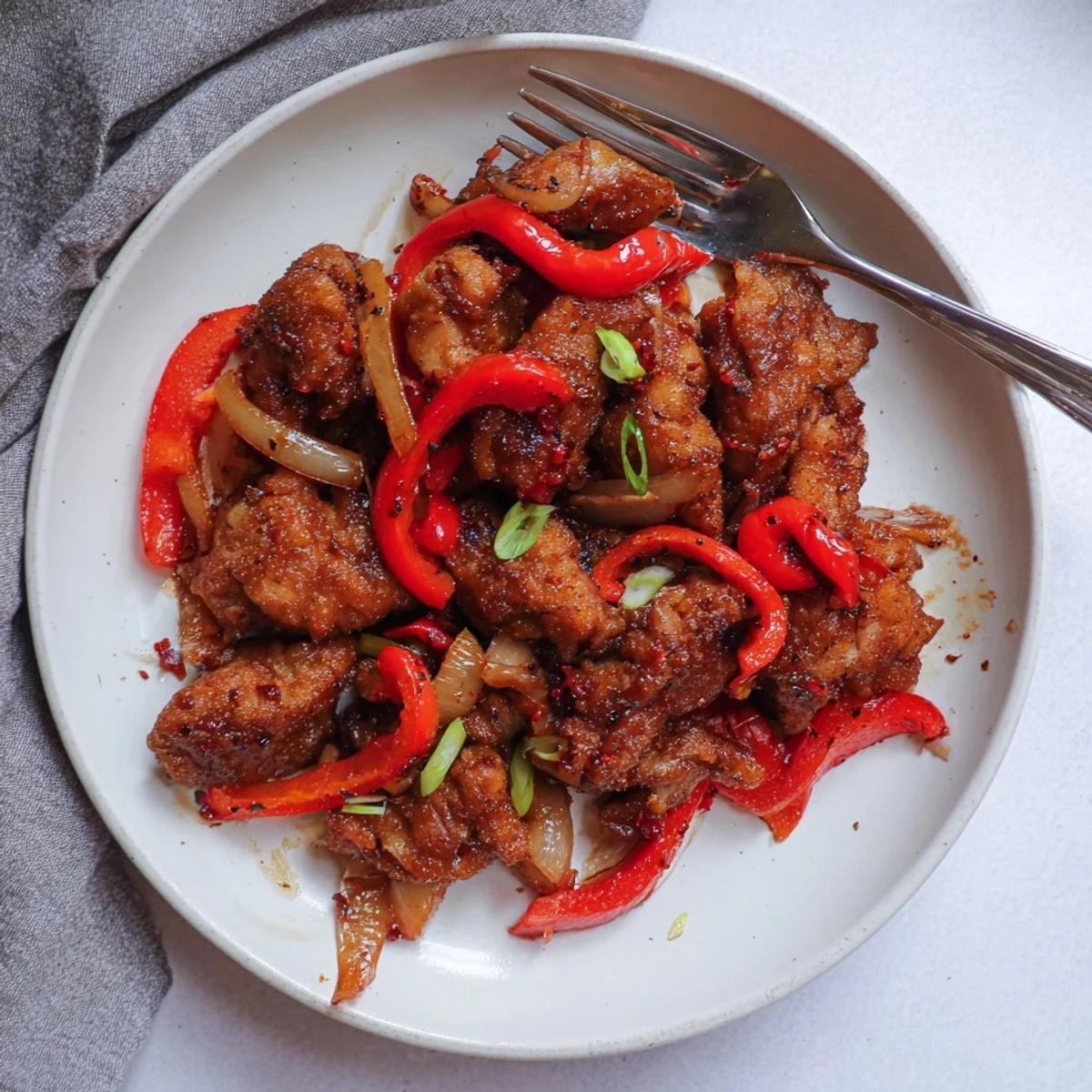 Asian-inspired crispy pepper chicken plated with sliced onions and fresh green onion garnish