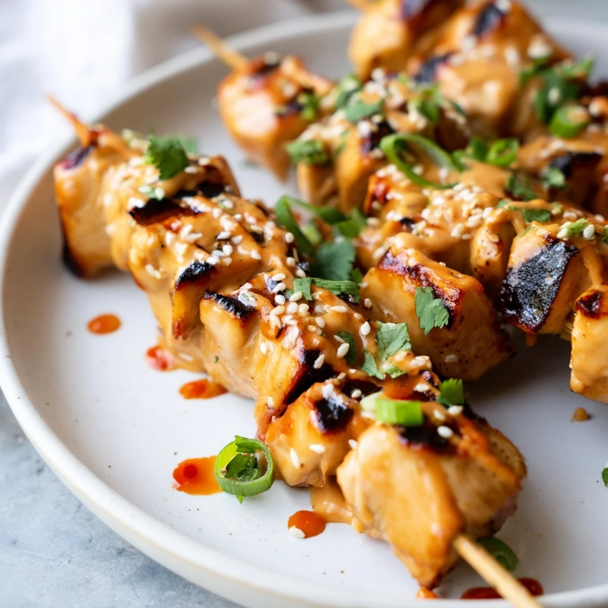 Juicy Bang Bang chicken skewers on a plate topped with scallions and cilantro garnish