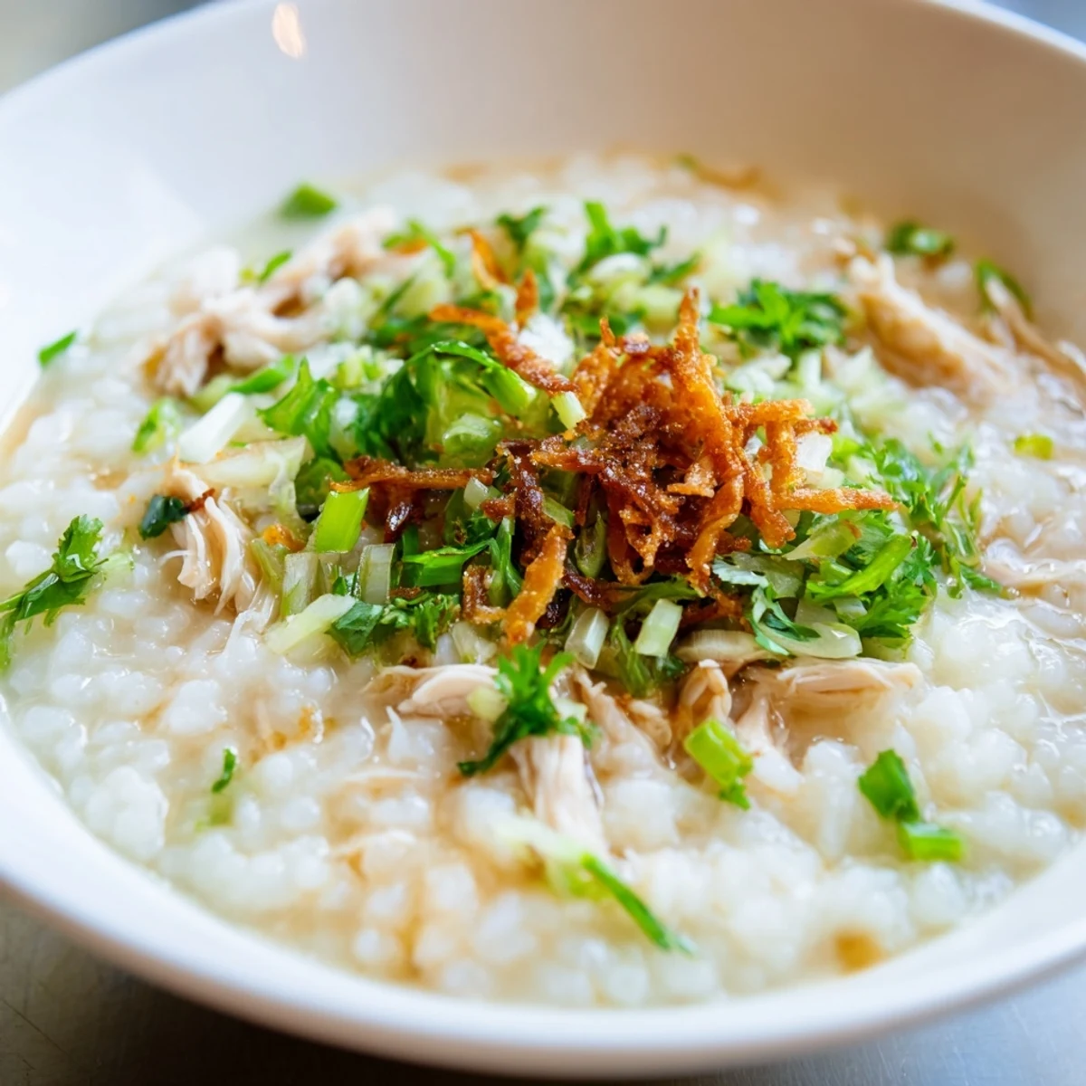 Creamy chao ga porridge featuring tender shredded chicken garnished with scallions and fragrant herbs