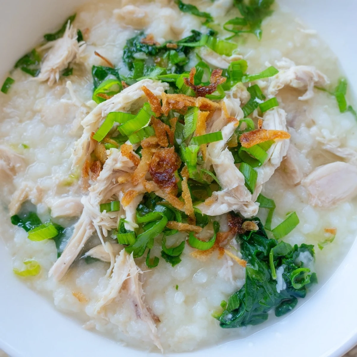 Comforting chicken rice porridge in a white bowl with lime wedges and optional chili oil