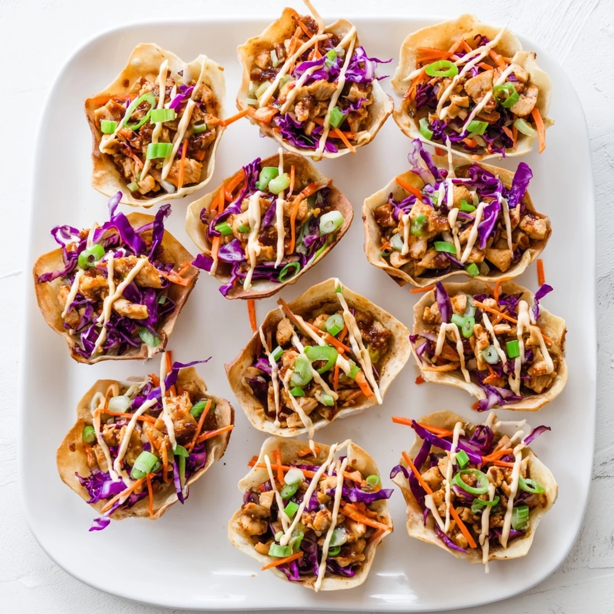 Golden chicken wonton tacos piled high with colorful crunchy slaw and spicy sriracha mayo drizzle