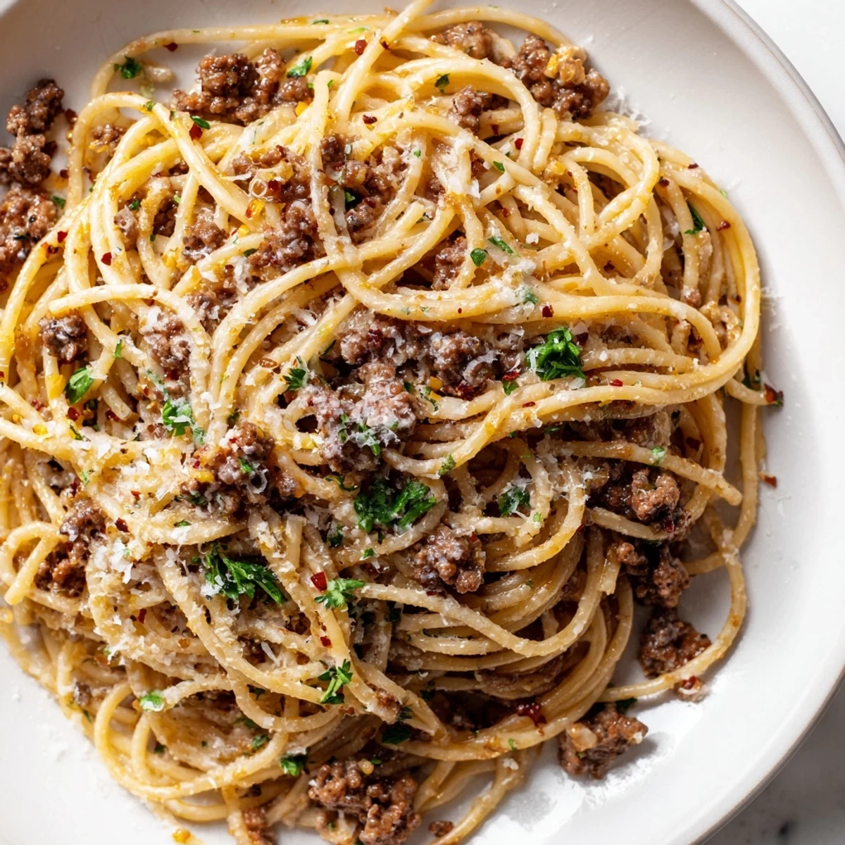 Steaming plate of garlic butter pasta with ground beef coated in rich, silky sauce