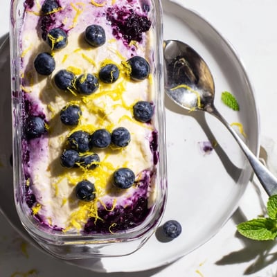 A spoon dips into creamy Lemon Blueberry Mousse, layered with a vibrant purple compote and lemon zest.