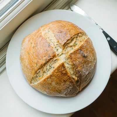 Freshly baked No Knead Dill Gouda Artisan Bread on a wooden board, perfect for pairing with a hot bowl of soup.